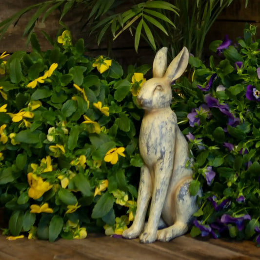 Decorative rabbit statue in front of green foliage with yellow and purple flowers