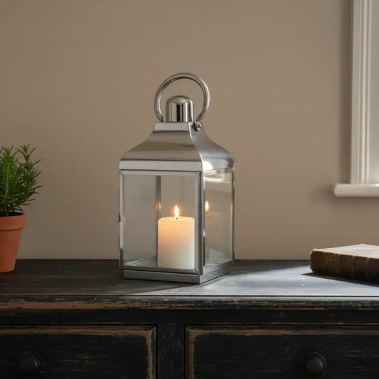 Silver lantern with a candle on a wooden surface against a beige wall