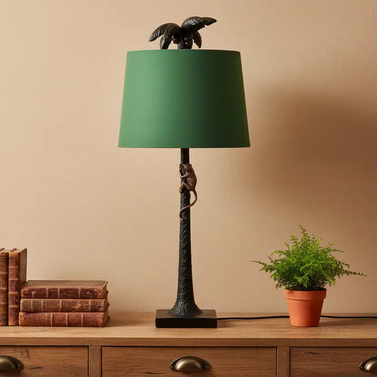 Decorative table lamp with green shade on a wooden surface with books and a plant.