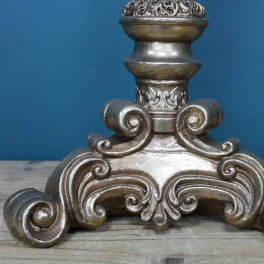 Decorative metal finial with intricate designs on a wooden surface against a blue background