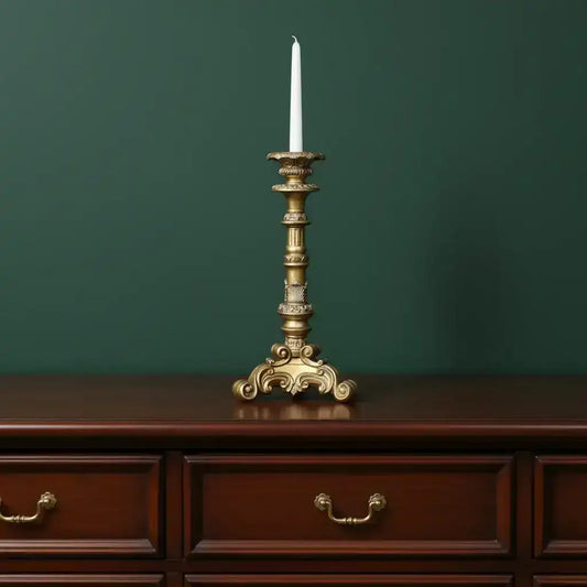 Decorative gold candlestick with a white candle on a wooden dresser against a green wall