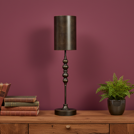 Decorative table lamp with a dark finish on a wooden surface against a purple wall.