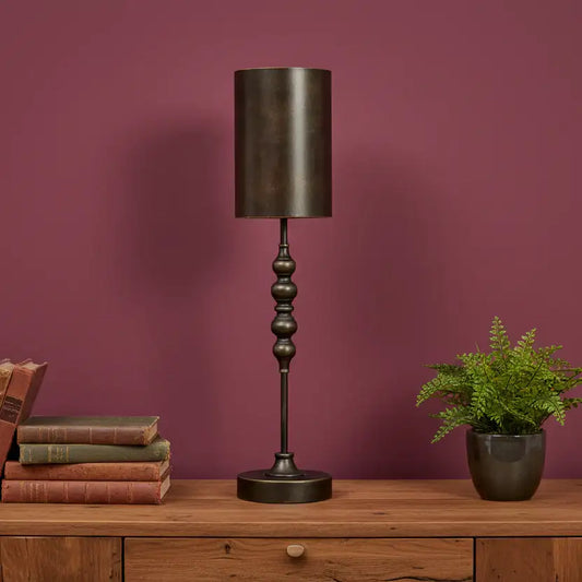 Decorative table lamp with a dark finish on a wooden surface against a purple wall.