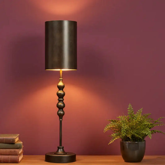Decorative table lamp with a black shade on a wooden surface against a purple wall.