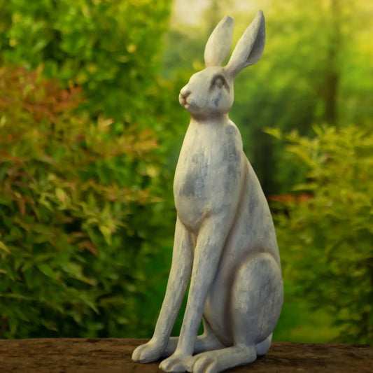 Statue of a rabbit sitting on a wooden surface with a blurred green natural background
