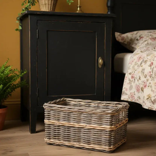 Black wooden cabinet with a wicker basket on a wooden floor next to a bed with floral bedding.