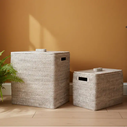 Two woven storage baskets with lids on a wooden floor against an orange wall.