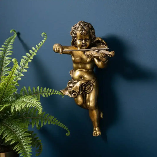 Bronze statue of a child playing a violin against a blue wall with a plant to the left.