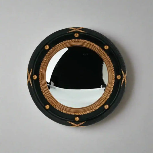 Round mirror with black frame and gold decorative elements on a plain wall.