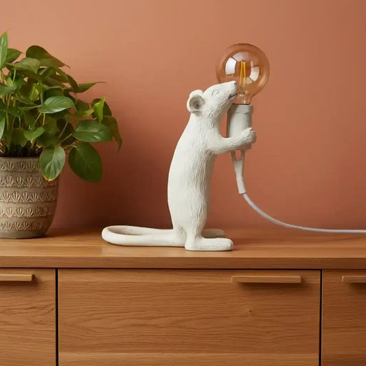 Decorative rat sculpture holding a light bulb on a wooden surface.