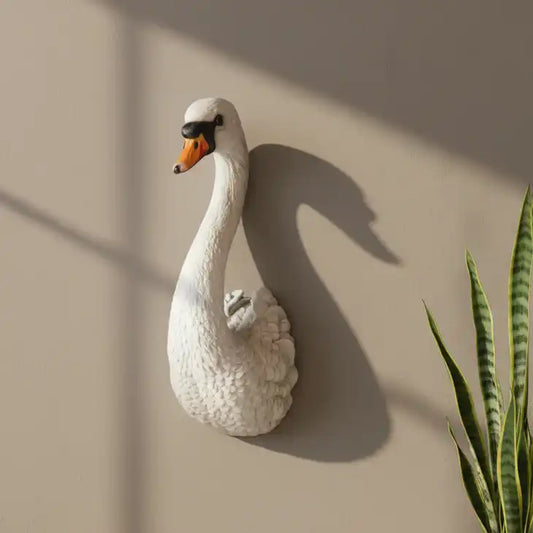 White swan wall sculpture on a beige wall with a plant to the right.