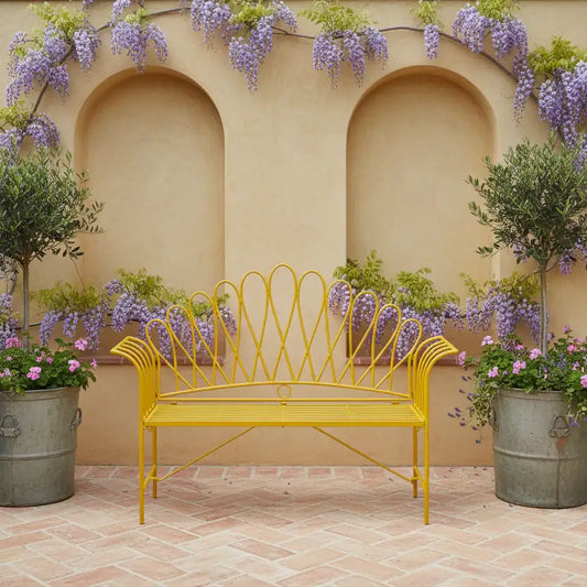 Yellow metal bench in a garden setting with flowers and a beige wall.