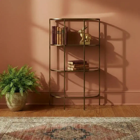Gold metal bookshelf against a pink wall with books and a plant.