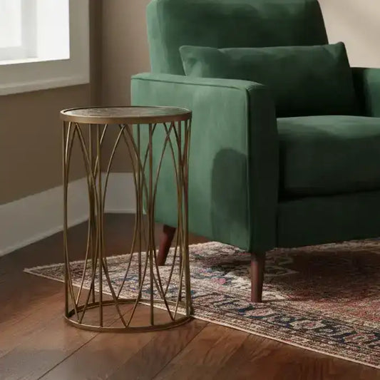 Gold side table next to a green armchair in a room with wooden flooring and a window.
