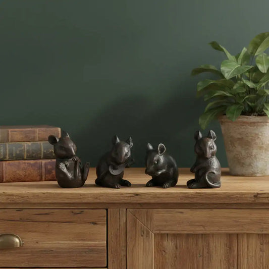 Four small black animal figurines on a wooden surface with a plant and books in the background.