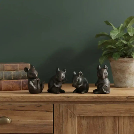 Four small black animal figurines on a wooden surface with a plant and books in the background.