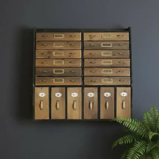 Wooden drawer unit with brass handles against a dark gray wall, accompanied by a potted fern.