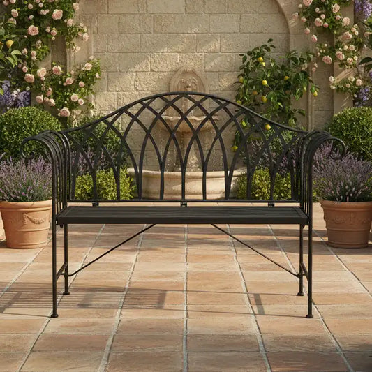 Wrought iron bench on a patio with a fountain and flowers in the background