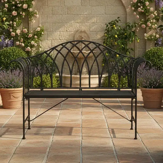 Wrought iron bench on a patio with a fountain and flowers in the background