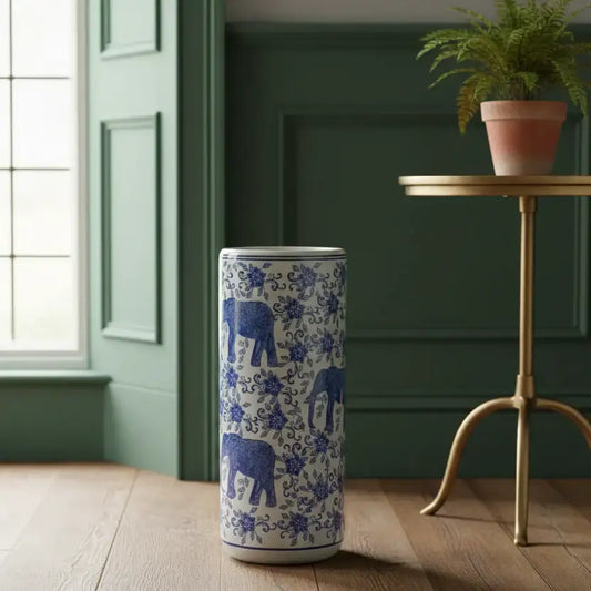 Tall cylindrical container with blue elephant design on a wooden floor next to a green wall and small table with a plant.