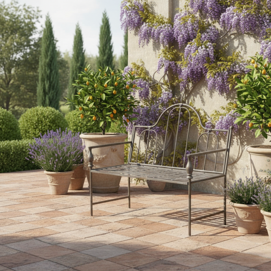Metal bench on a patio with potted plants and a wisteria-covered wall.