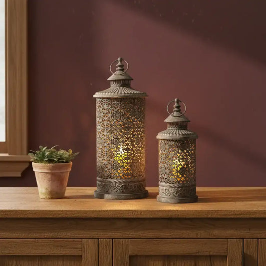 Decorative lanterns on a wooden surface with a potted plant against a maroon wall.