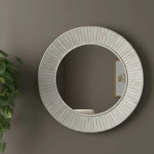 Round decorative mirror with a textured frame on a wall, next to a plant.