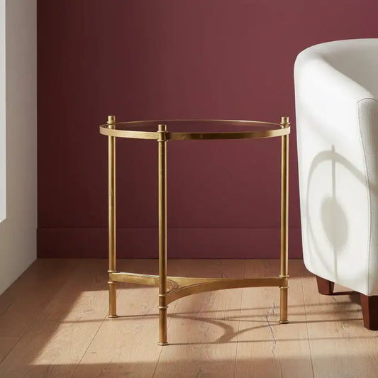 Gold side table with glass top in a room with a white chair and purple wall.