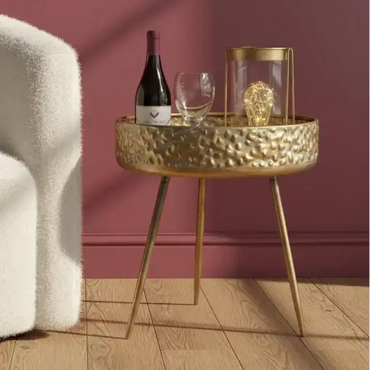 Gold side table with wine bottle, glasses, and decorative item against a red wall.