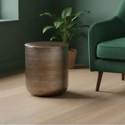 Bronze side table next to a green armchair in a room with a plant.