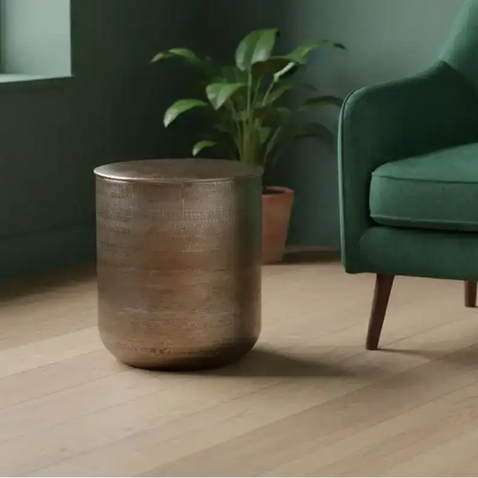Bronze side table next to a green armchair in a room with a plant.