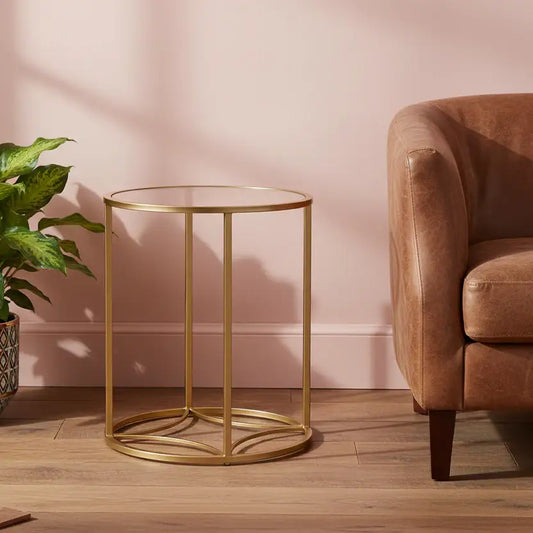 Gold side table in a living room with a pink wall and brown armchair.