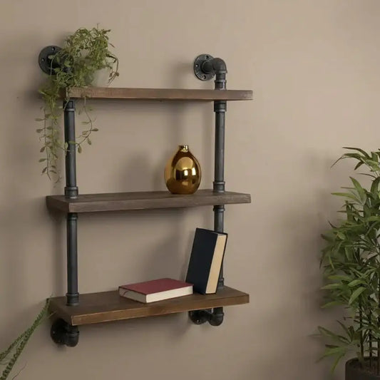 Wooden shelf with metal pipes against a beige wall, decorated with books and a gold vase.