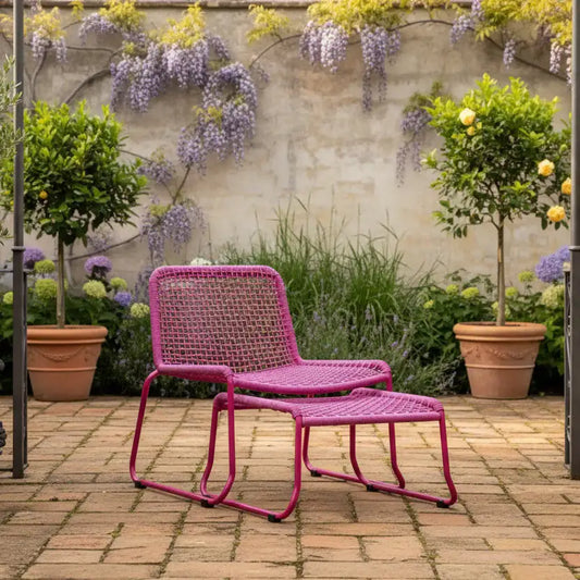 Pink outdoor chair and ottoman with a garden setting featuring plants and flowers.