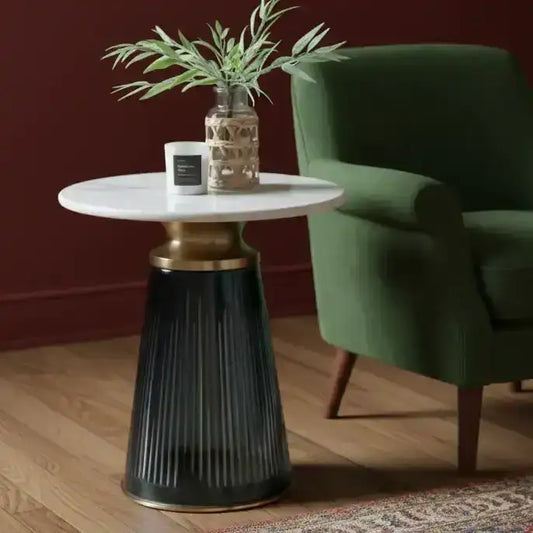 Round side table with marble top and black base next to a green armchair in a room.