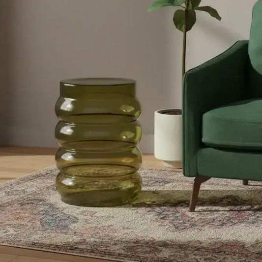 Green glass side table next to a green armchair in a living room setting.