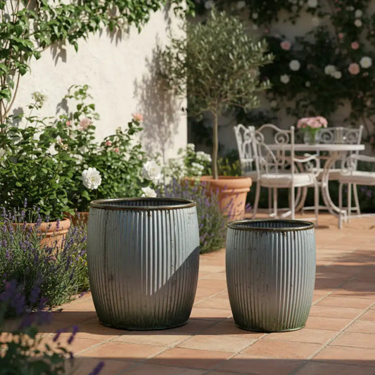 Two gray planters on a patio with garden and table in the background