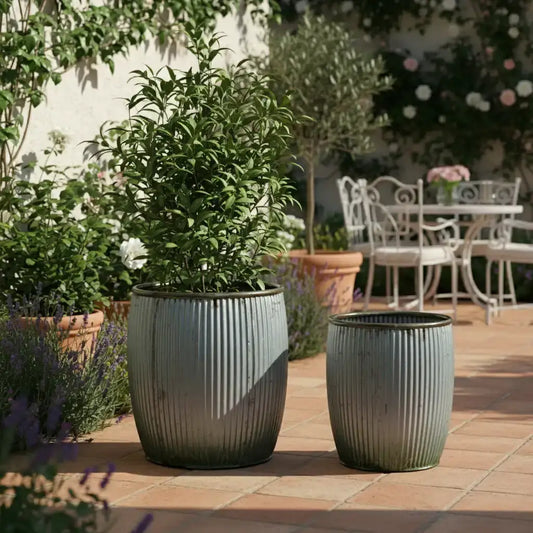 Two gray planters with green plants on a patio with outdoor furniture in the background.