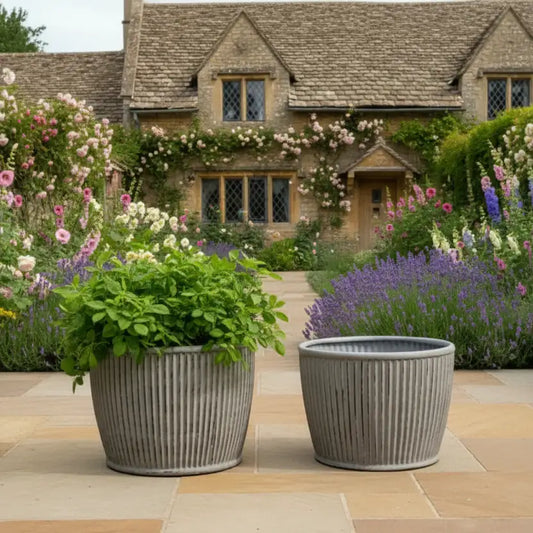 Two gray planters with greenery in front of a charming house with floral decorations.
