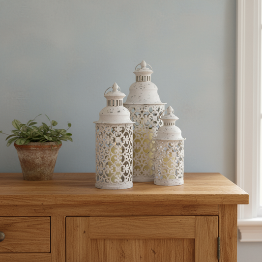 Three decorative lanterns on a wooden surface with a plant in the background