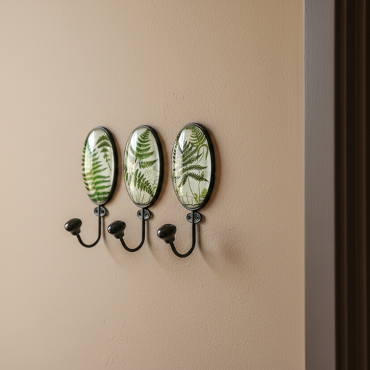 Wall-mounted hook with three decorative plates featuring fern designs on a beige wall.