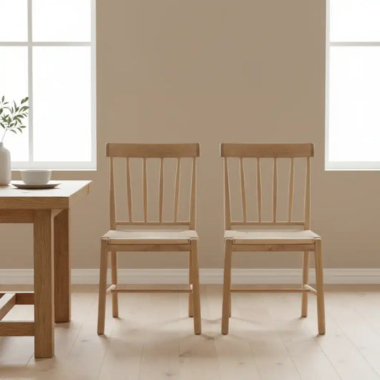 Two wooden chairs in a room with a table and windows.