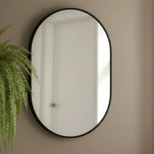 Round mirror with black frame on a beige wall next to a green plant