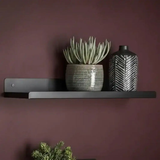 Black shelf with a potted plant and a black and white vase against a purple wall