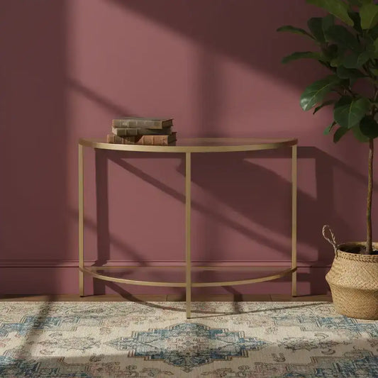 Gold console table against a pink wall with a plant and books on it