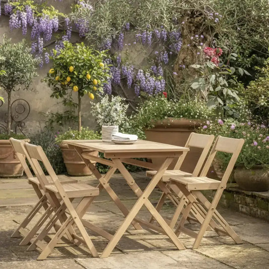 Wooden outdoor dining set with chairs on a wooden deck surrounded by flowers and plants.