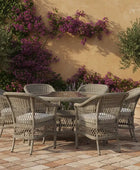 Outdoor patio set with wicker chairs and table on a stone patio, surrounded by plants and flowers.