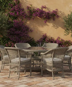 Outdoor patio set with wicker chairs and table against a wall with purple flowers.