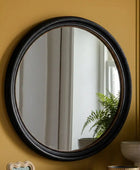 Round mirror with black frame on a yellow wall