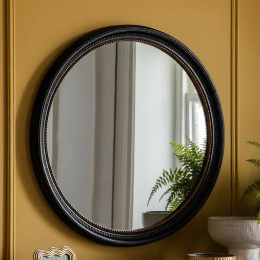 Round mirror with black frame on a yellow wall
